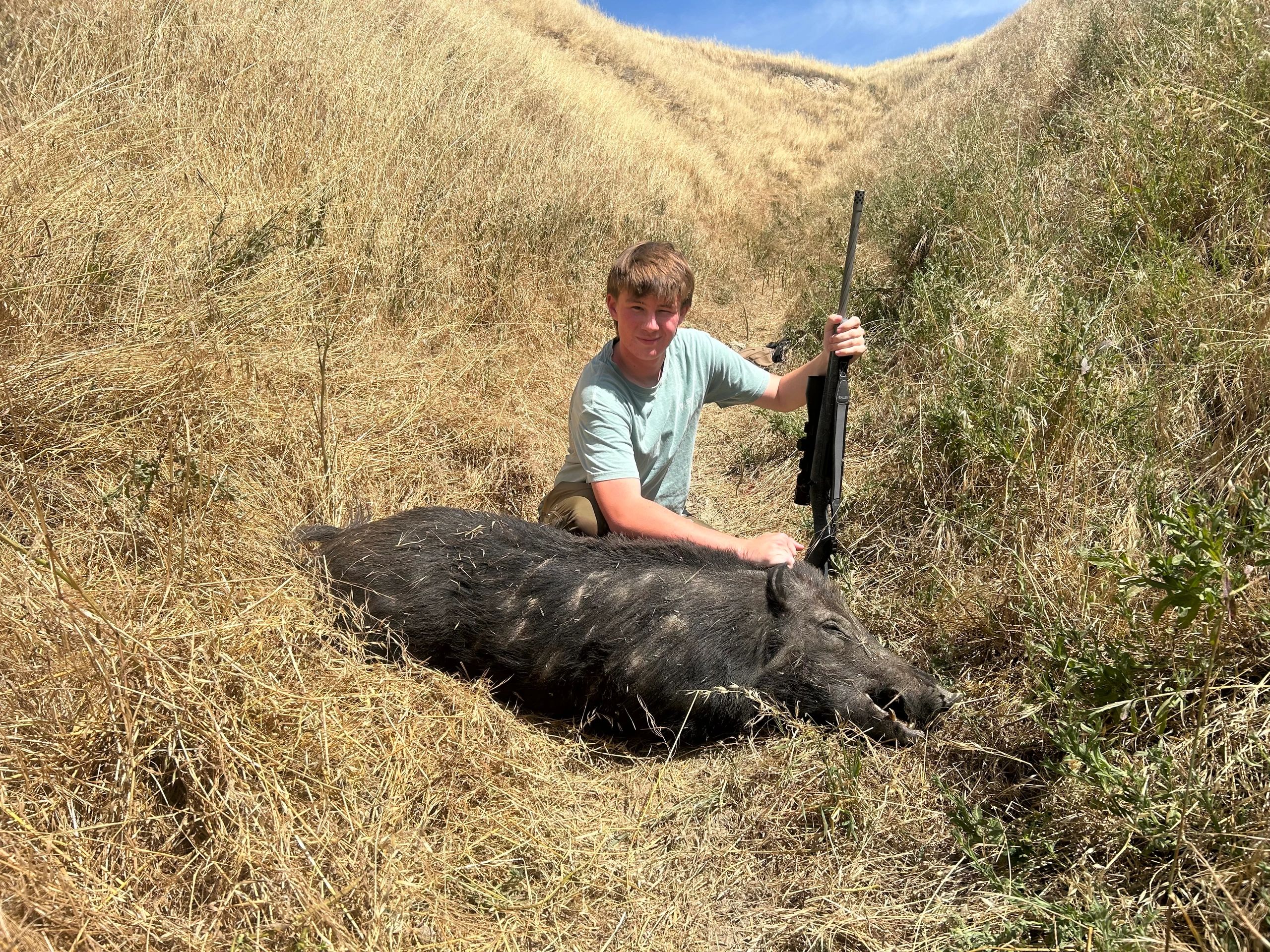 Young hunter with harvested wild boar on hillside